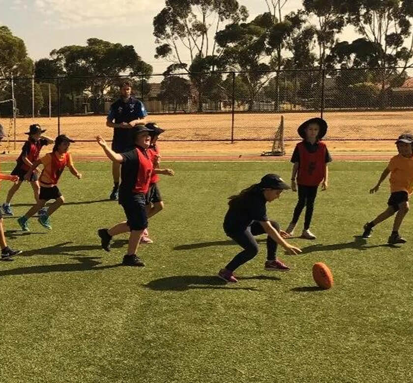 Image (An NLS coach handing a marker to a group of primary school children sitting on the grass) (2) (1)