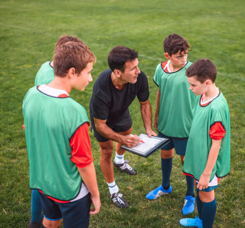 Image (An NLS coach handing a marker to a group of primary school children sitting on the grass) (3) (1)